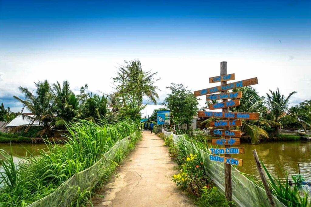 Landelijk weggetje op Con Chim-eiland in Tra Vinh met palmbomen, waterkanalen en houten wegwijzers naar lokale eetgelegenheden