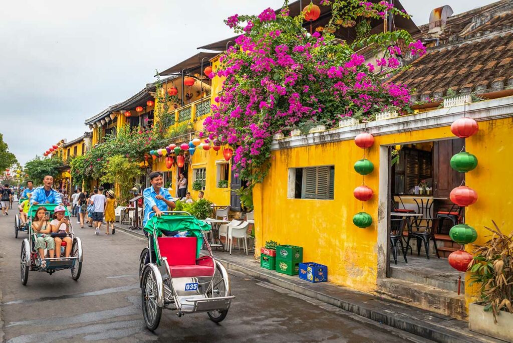 Cyclo riskja rijdt door Hoi An Ancient Town met kleurrijke lantaarns en gele huizen
