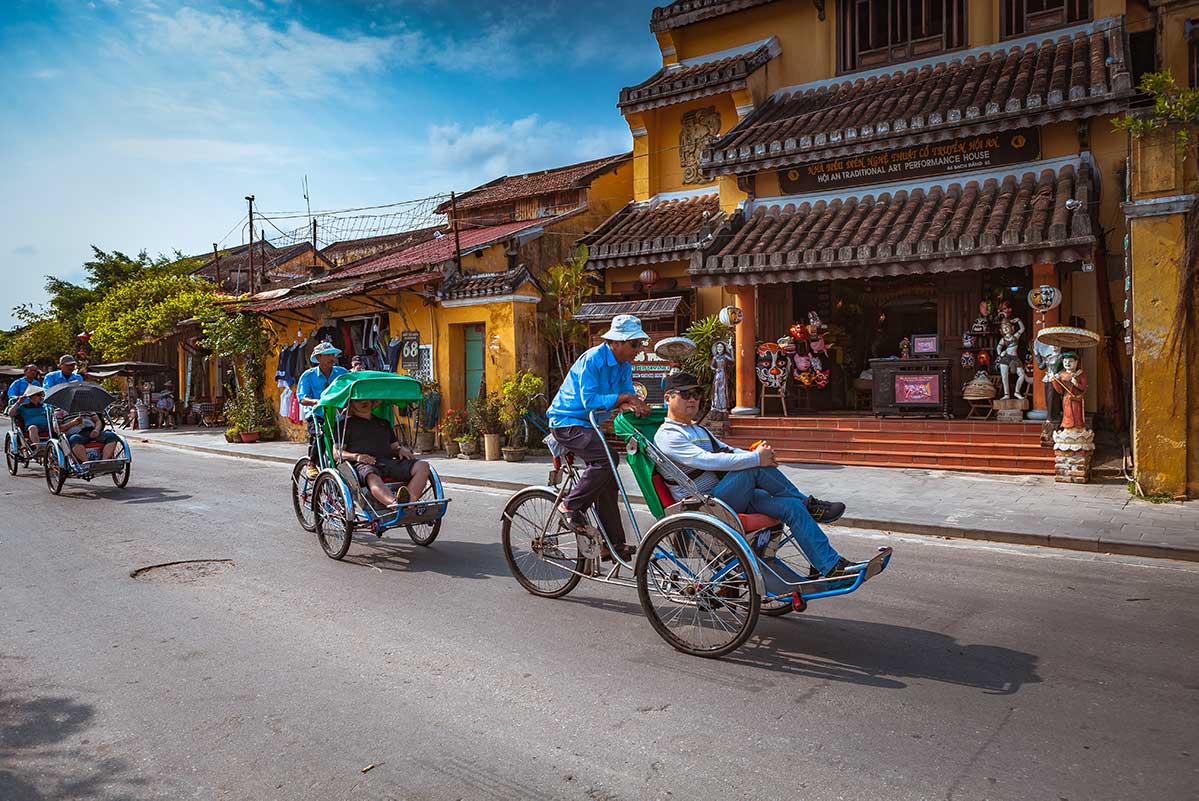 Cyclo riskja met passagiers in de oude straat van Hoi An langs gele historische gebouwen