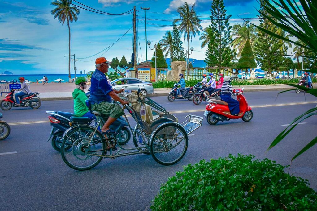Cyclo riskja rijdt langs de boulevard van Nha Trang met uitzicht op zee en palmbomen