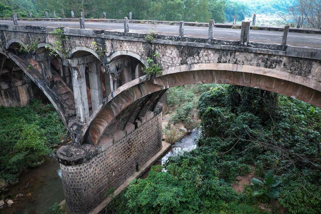 Oude stenen brug bij de historische Ho Chi Minh Trail, verscholen in groen landschap en herinnerend aan de logistieke routes uit de Vietnamoorlog.
