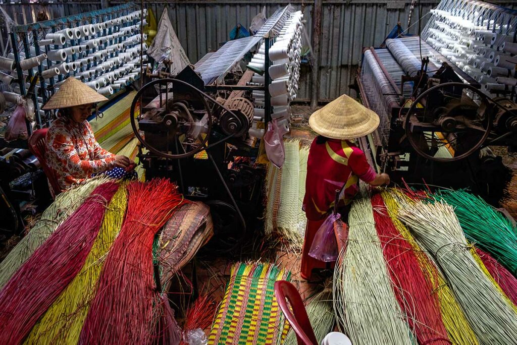 Vrouwen weven kleurrijke biezen matten op traditionele weefgetouwen in Dinh Yen mattenweefdorp bij Sa Dec in de Mekong Delta