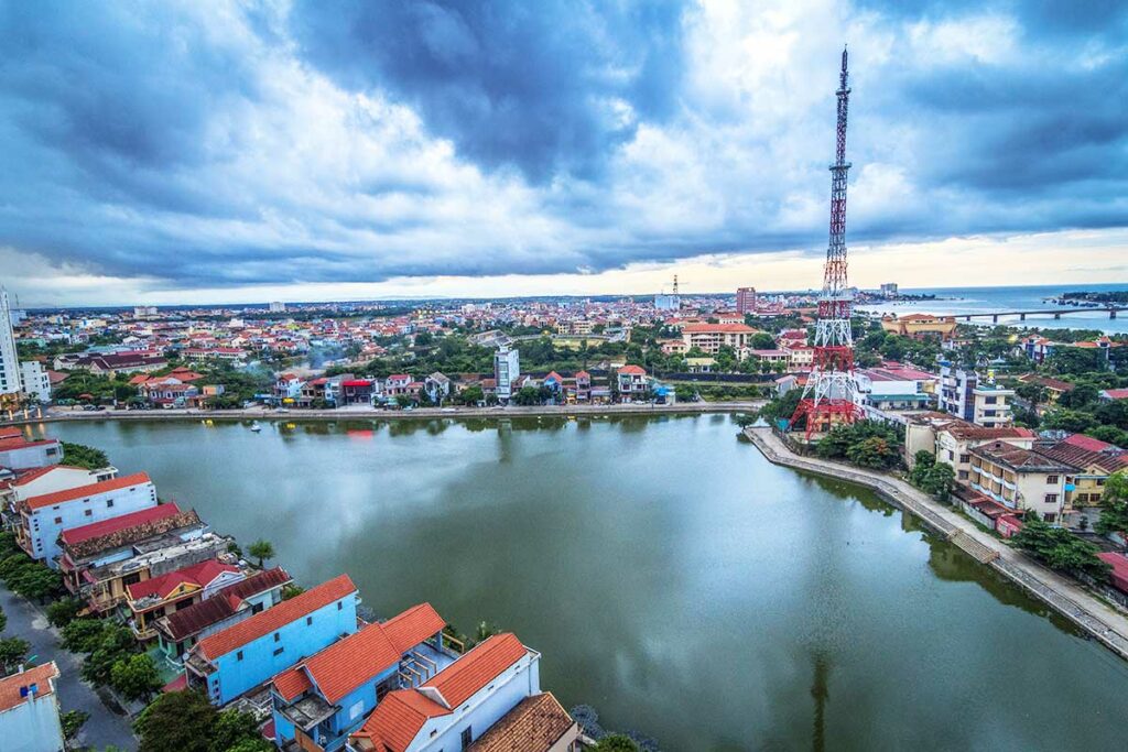 Uitzicht over Dong Hoi met de rivier, woonwijken en de karakteristieke zendmast, gezien vanaf boven bij bewolkt weer.