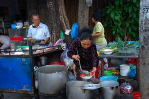 Ouder echtpaar dat noedelsoep serveert vanuit een eenvoudige straatkeuken, een herkenbaar tafereel binnen street food in Vietnam