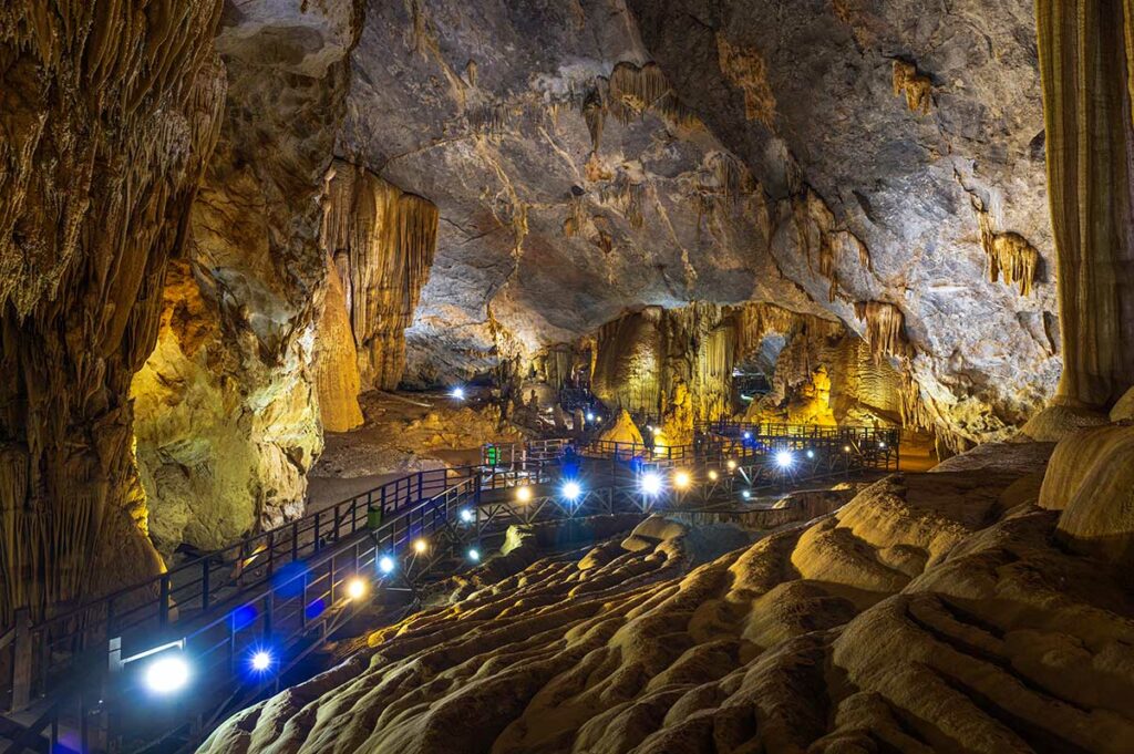Verlichte kalksteenformaties en houten loopbrug in Paradise Cave (Thien Duong) in Phong Nha, met grote stalactieten en stalagmieten in een brede grotzaal.