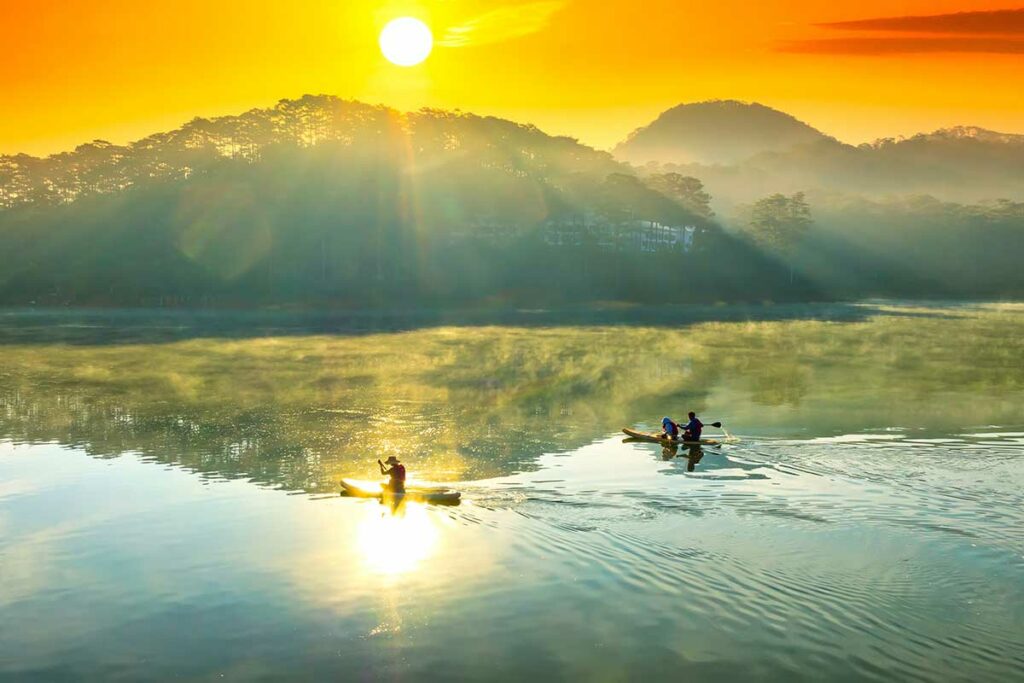 Kajakkers op Tuyen Lam Lake bij zonsopkomst in Da Lat, met mist en zacht licht, ideaal voor natuur- en landschapsfotografie.