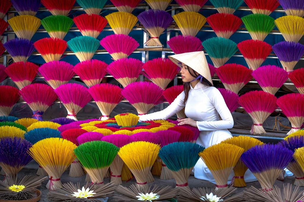 Vrouw in traditionele kleding tussen kleurrijke wierookbundels in een dorp bij Hue, een populaire locatie voor creatieve en culturele fotografie in Vietnam.