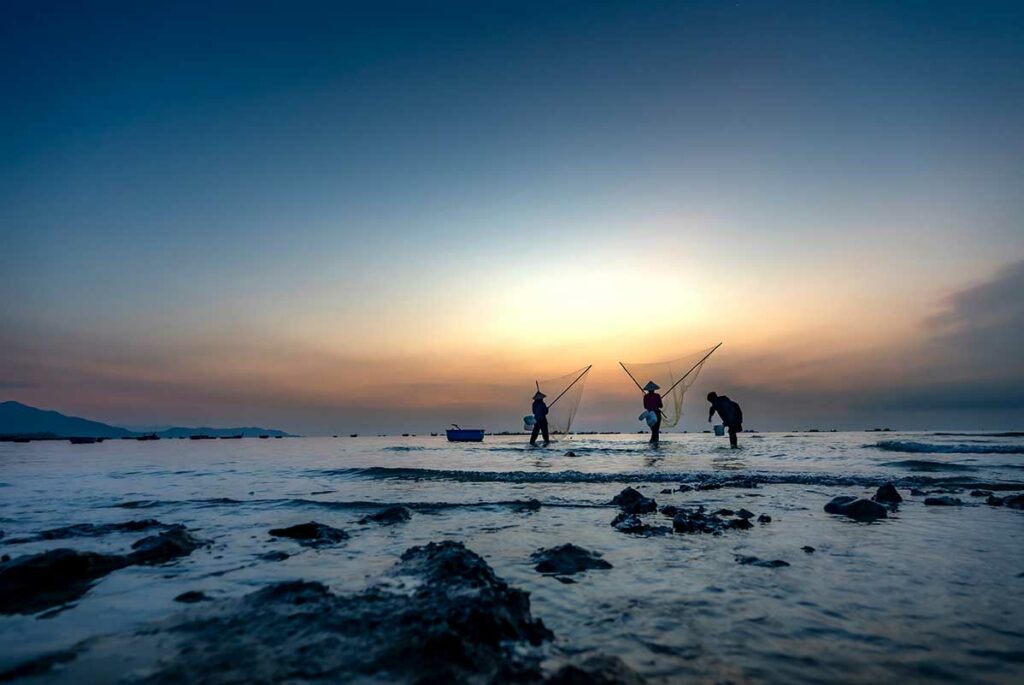 Vissers werken in ondiep water langs de kust van Phu Yen bij zonsopkomst, een sfeervol tafereel voor documentaire en reisfotografie in Vietnam.