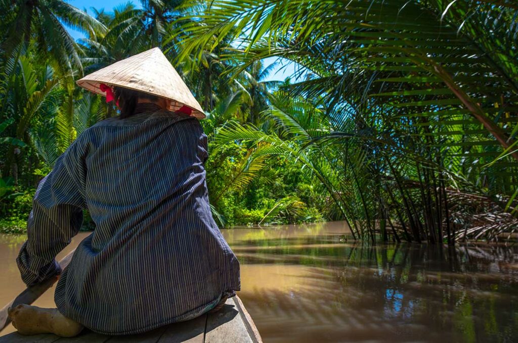 Lokale vrouw vaart met een sampan door een smalle mangrovekreek in de Mekongdelta, een rustig moment voor documentaire en reisfotografie in Zuid-Vietnam.