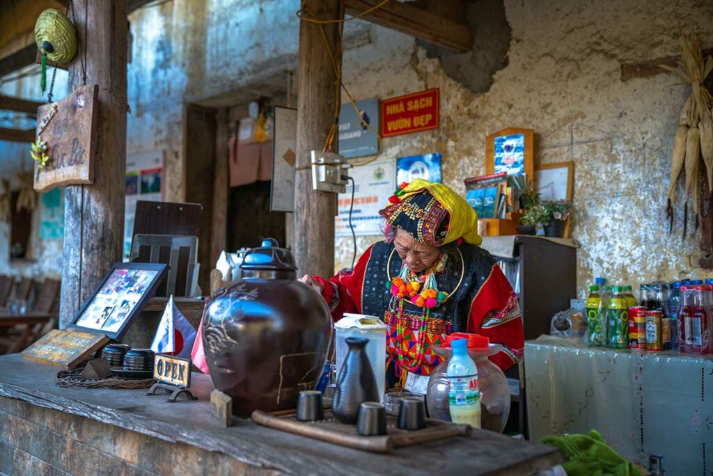 Etnische vrouw in traditionele kleding bereidt drank in een klein dorpscafé in Ha Giang, ideaal voor culturele en reportagefotografie in Vietnam.