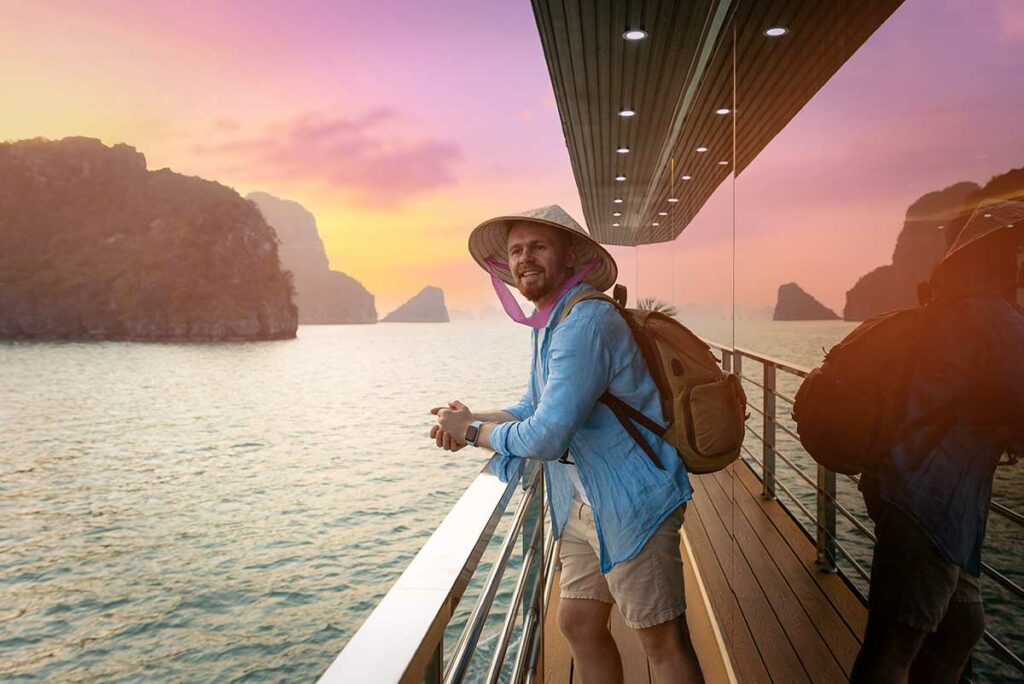 Reiziger staat op het dek van een cruiseboot in Halong Bay bij zonsondergang, een ontspannen moment voor reis- en landschapsfotografie in Vietnam.