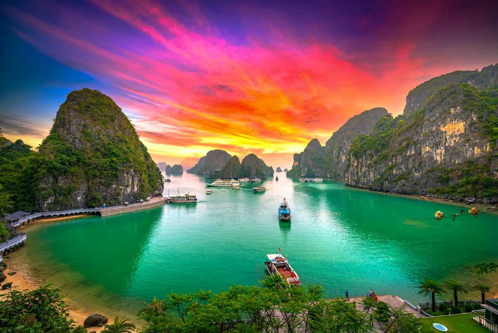 Halong Bay bij zonsondergang met felgekleurde lucht en boten tussen de eilanden, een populair moment voor avond- en reisfotografie.