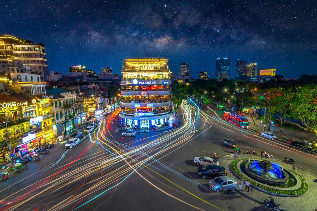Nachtfotografie in Hanoi met lichtsporen van verkeer rond een druk kruispunt, ideaal voorbeeld van straatfotografie in Vietnam bij avondlicht.