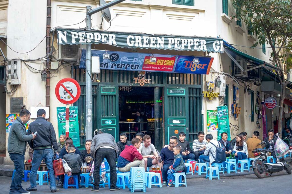 Straatbeeld in de Old Quarter van Hanoi waar locals en reizigers bia hoi bier drinken op lage plastic krukjes, typisch voorbeeld van Vietnamese biercultuur