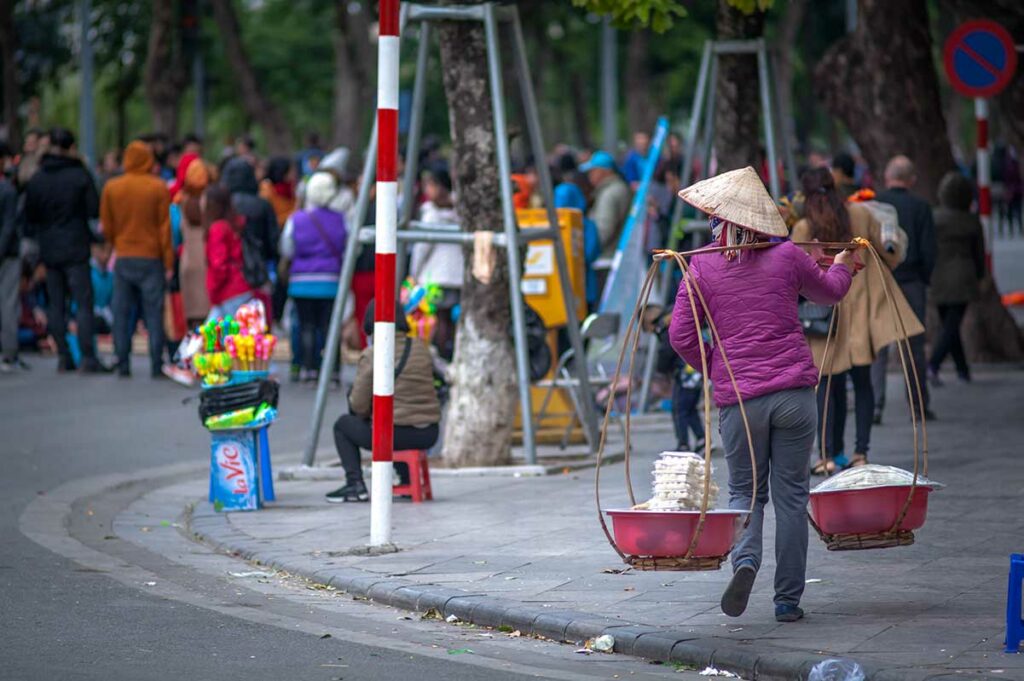 Straatbeeld in Hanoi in de winter met lokale straatverkoper en mensen in warme kleding langs een brede boulevard