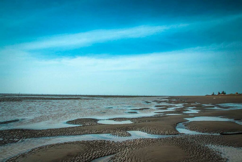 Laagwater bij Ho Be Beach in Soc Trang met modderige zandpatronen en ondiepe getijdenpoelen onder blauwe lucht