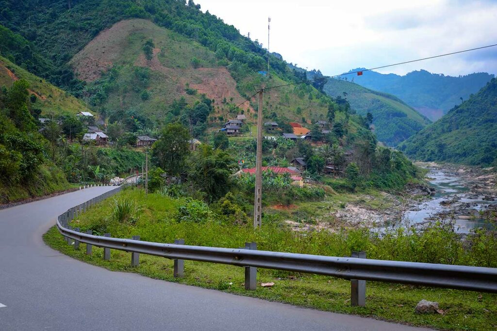 Afgelegen traject van de Ho Chi Minh Road door een rivierdal en bergachtig landschap, met kleine dorpen langs de route.