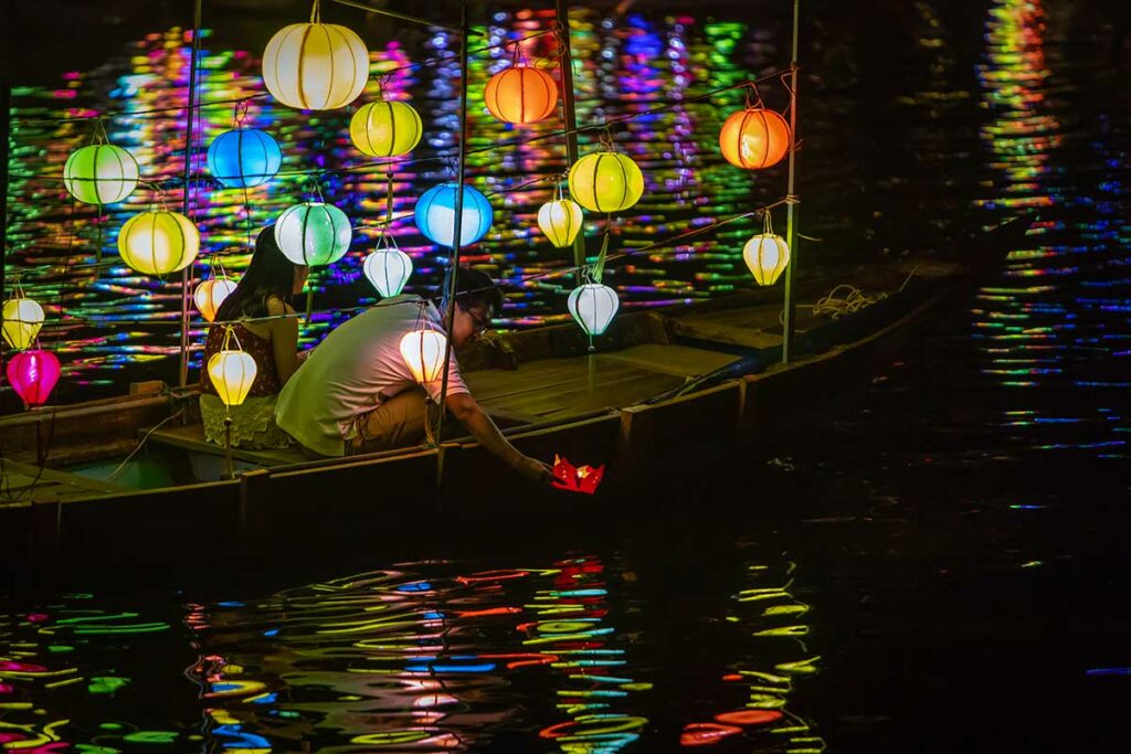 Bezoekers laten papieren drijvende lampionnen te water vanaf een houten boot tijdens het Hoi An Lantern Festival