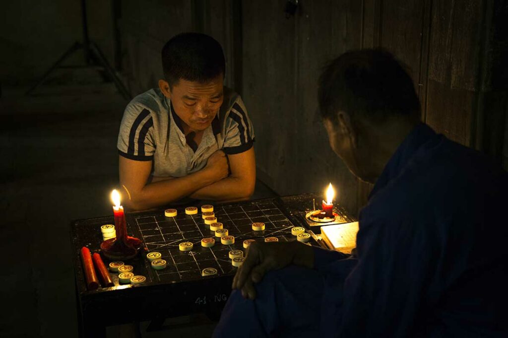 Lokale mannen spelen Xiangqi bij kaarslicht tijdens het Hoi An Lantern Festival in de oude binnenstad van Hoi An