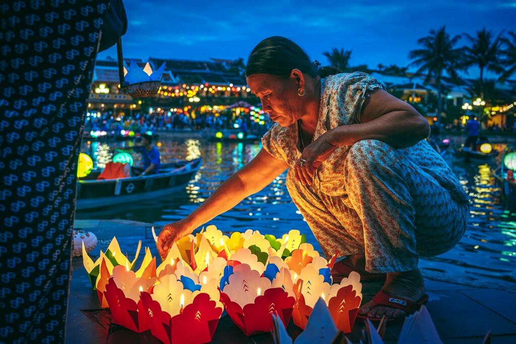 Lokale vrouw plaatst kleurrijke lantaarns op de rivier in Hoi An tijdens de avond, een sfeervol moment voor nacht- en reisfotografie in Vietnam.