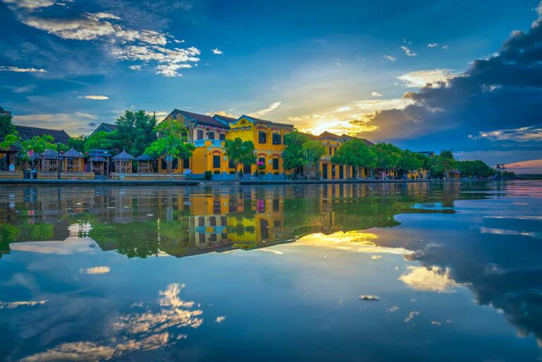 Weerspiegeling van historische huizen langs de rivier in Hoi An bij zonsondergang, ideaal voor architectuur- en landschapsfotografie.