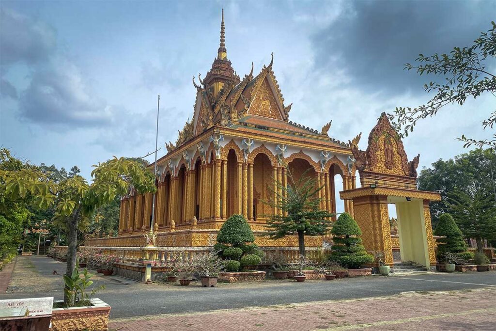 Kampong Ksan Pagoda in Tra Vinh met goudkleurige Khmer-architectuur en rijk versierde gevel onder een bewolkte hemel
