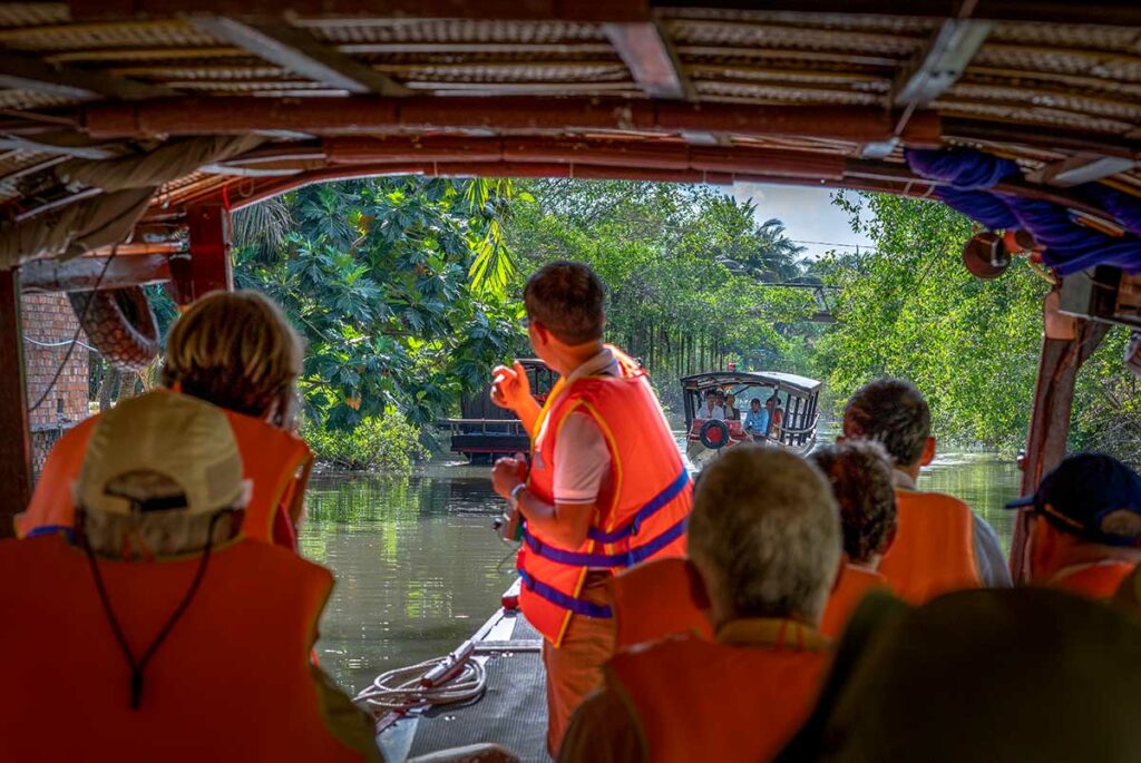 Toeristen met reddingsvest tijdens een boottocht door een smal kanaal bij Sa Dec