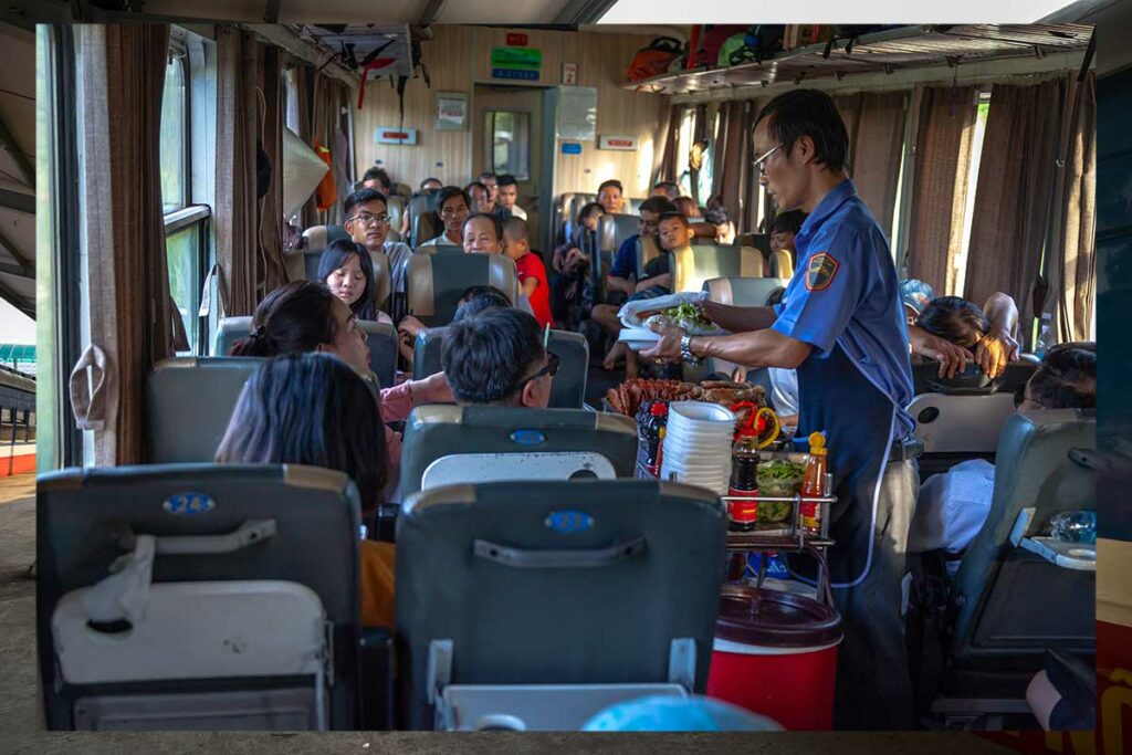Treinpersoneel met karretje vol snacks en drinken in Vietnamese trein met passagiers op soft seats