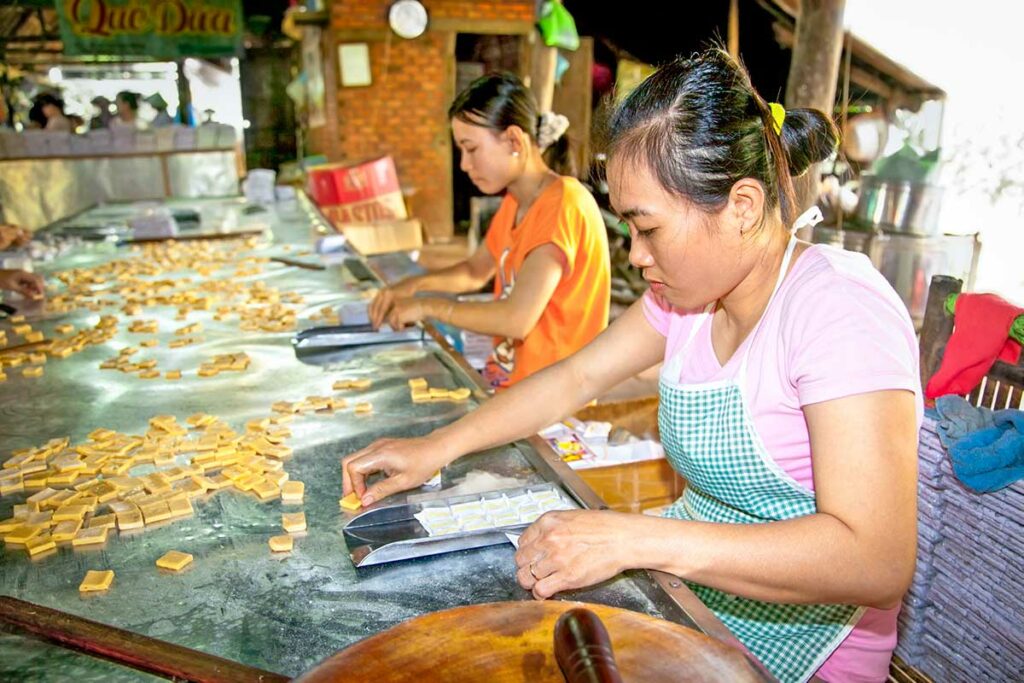 Vrouwen bereiden en snijden kokosnootsnoepjes in een traditionele kokosnootfabriek in Ben Tre, Mekong Delta – kokosnootproductie Mekong Delta