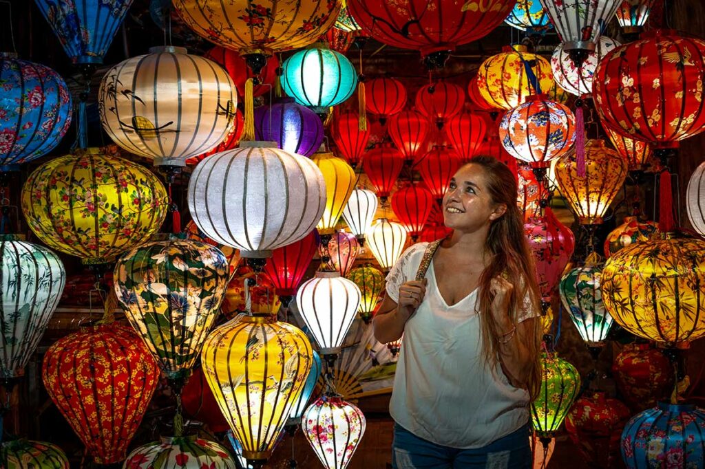 Toerist tussen kleurrijke zijden lampionnen in een winkel tijdens het Hoi An Lantern Festival in de oude stad