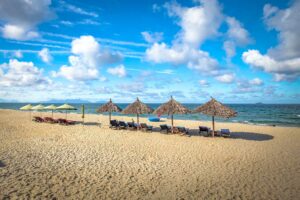 Rieten strandparasols en ligbedden op An Bang Beach bij Hoi An onder blauwe lucht