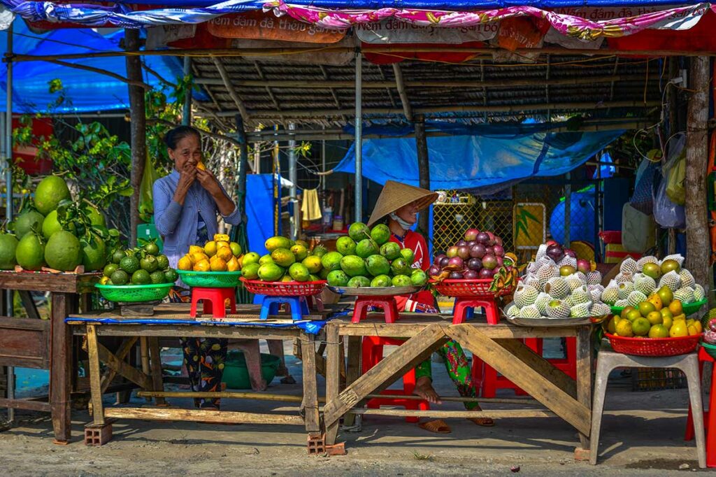 Fruitkraam op lokale markt in Soc Trang met mango’s citrusvruchten en verkoopsters in traditionele hoed