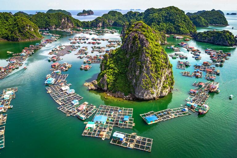 Luchtfoto van een drijvend vissersdorp in Lan Ha Bay, met kleurrijke huisjes, viskwekerijen en kalkstenen eilanden verspreid over het heldergroene water