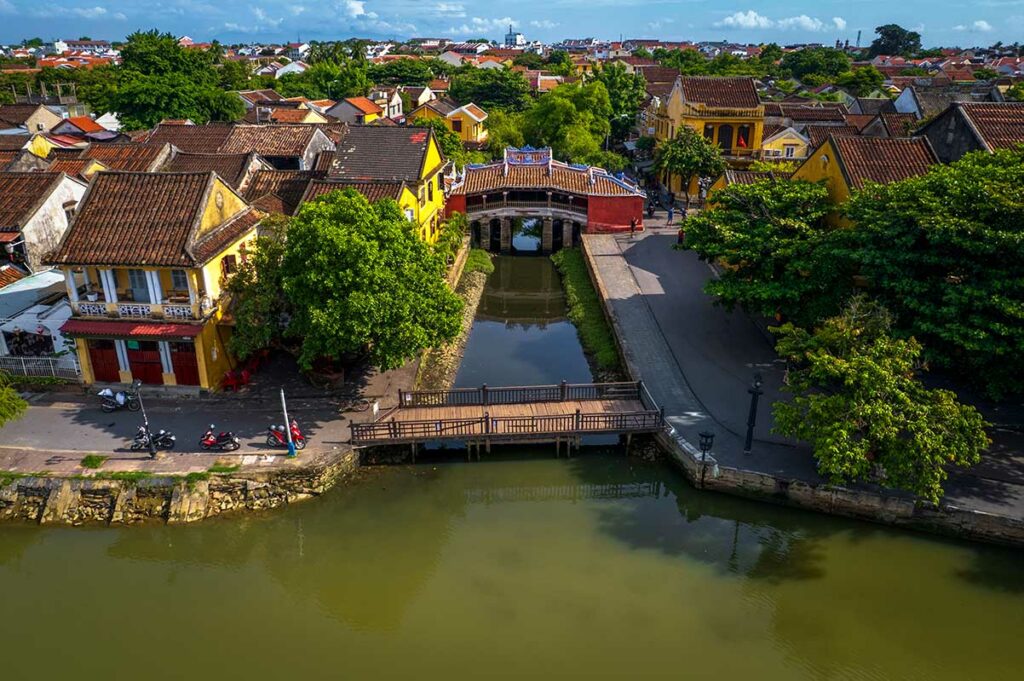 Luchtfoto van de Japanse Brug in Hoi An over smal kanaal tussen historische gele huizen in de oude stad