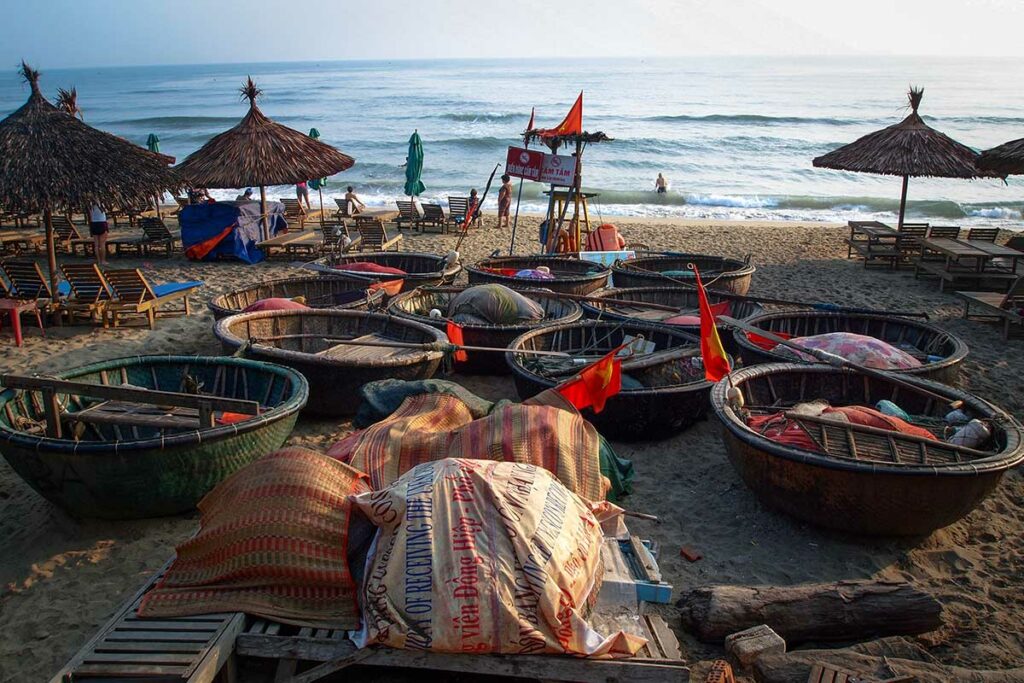 Ronde vissersboten op het strand van An Bang Beach bij Hoi An met zee en strandstoelen op de achtergrond