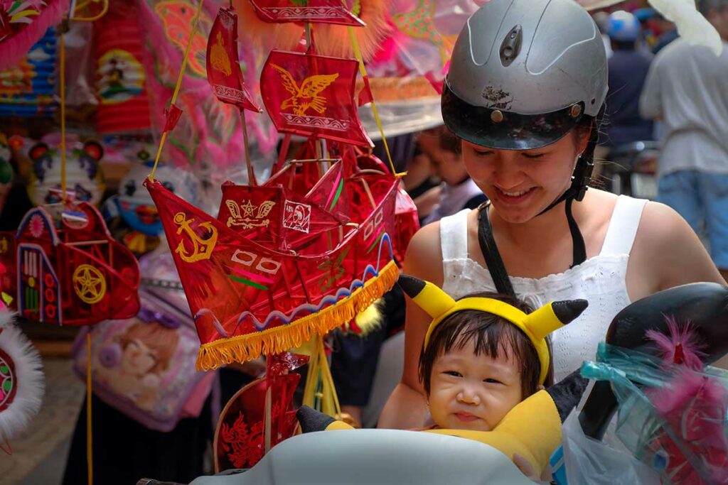 Kind met een traditionele lantaarn tijdens Tết Trung Thu in Vietnam, gefotografeerd op een drukke markt in de aanloop naar het Midherfstfestival.
