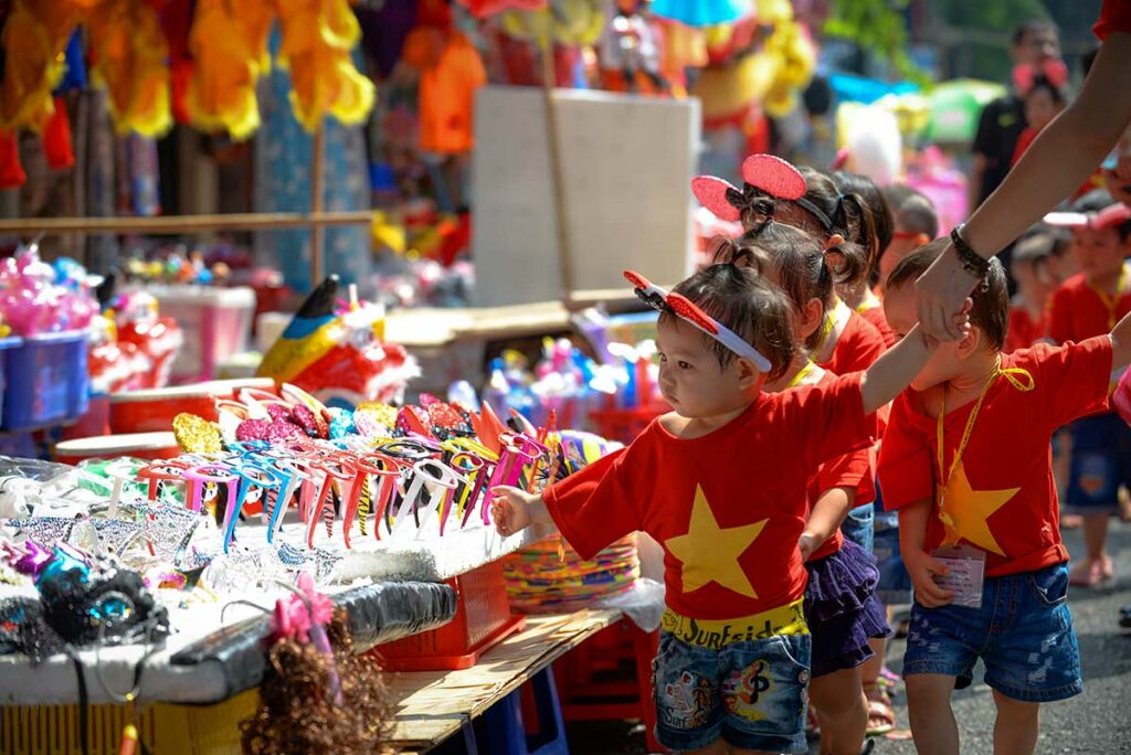 Kinderen vieren Tết Trung Thu in Vietnam bij een feestkraam, met speelgoed en decoraties die horen bij het Midherfstfestival.