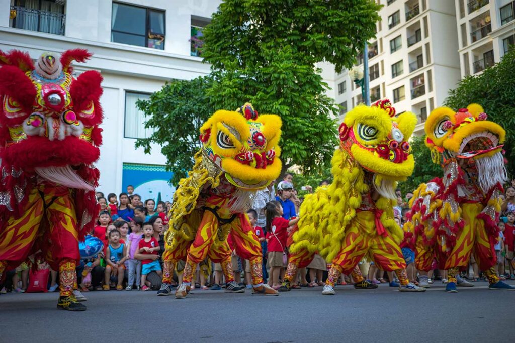 Groep leeuwendansers in kleurrijke kostuums tijdens het Mid-Autumn Festival in Vietnam, optreden voor een grote groep toeschouwers in een woonwijk.
