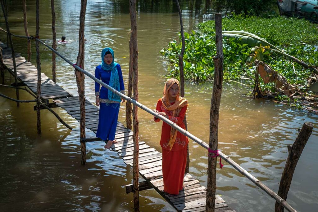Moslim vrouwen uit Cham dorp bij Chau Doc lopen over houten brug boven rivier in de Mekongdelta