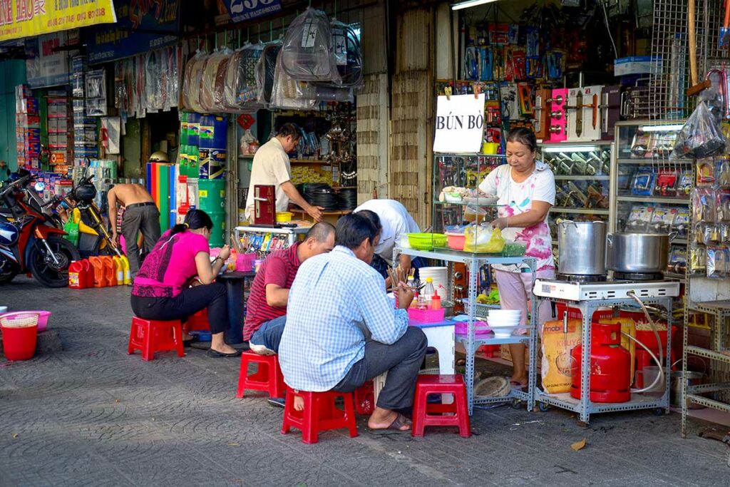 Locals eten noedelsoep (bún bò) op lage plastic krukjes in een steeg, een typisch beeld van street food in Vietnam
