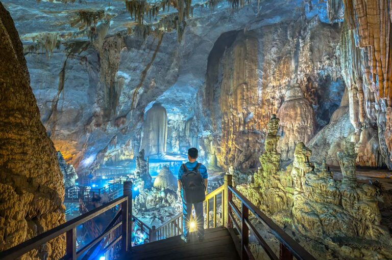 Bezoeker op een houten trap in Paradise Cave (Thien Duong) in Phong Nha, met zicht op enorme grot­zalen, hoge stalactieten en verlichte loopbruggen in de grot.