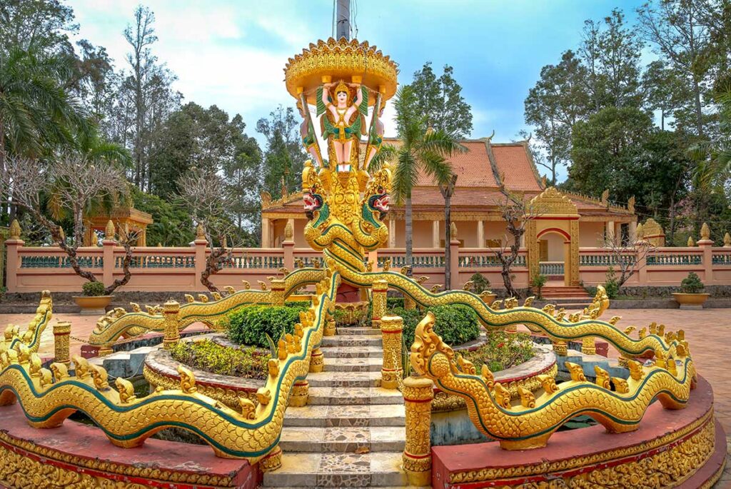 Gouden beeld en naga-slang bij Phat Lon Pagoda in Rach Gia met Khmer tempel op de achtergrond