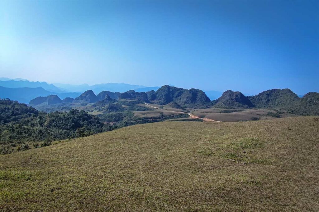Uitzicht over de Phan Thanh grasheuvels in Phia Oac National Park met glooiende heuvels, kalkstenen bergformaties en een afgelegen weg door het landschap in Cao Bang.