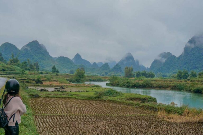 Reiziger met motor langs rijstvelden en rivier in Phong Nam Valley, Cao Bang, met karstbergen in de mist