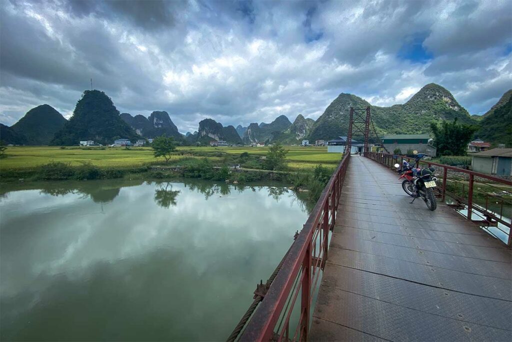 Brug over de Quay Son-rivier bij Ngoc Con in Phong Nam Valley, met rijstvelden en kalkstenen bergen op de achtergrond