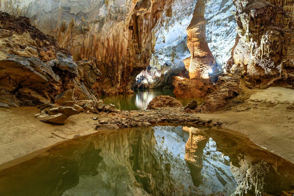 Ondergrondse rivier in Phong Nha Cave met reflecties van rotswanden en verlichting, zichtbaar tijdens het bezoek aan de grot.