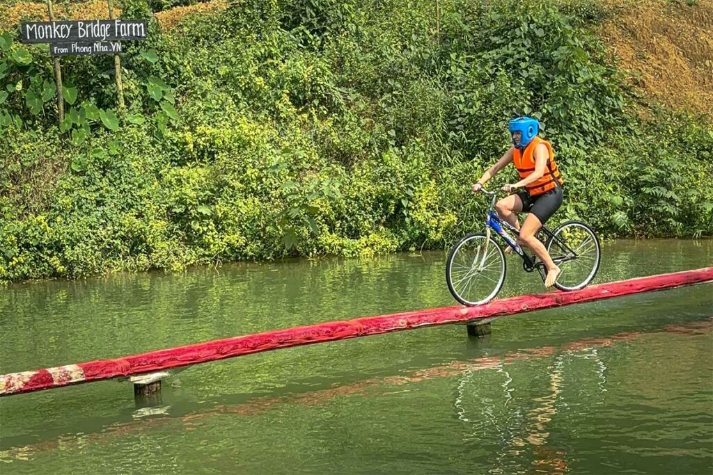 Bezoeker fietst over de smalle Monkey Bridge bij Phong Nha, een eenvoudige houten brug over de rivier in een landelijke omgeving.