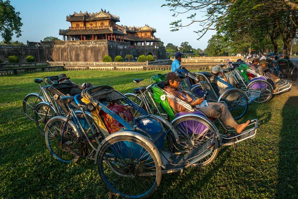 Cyclo riskja chauffeurs wachten bij de Keizerlijke Stad in Hue met de citadel op de achtergrond