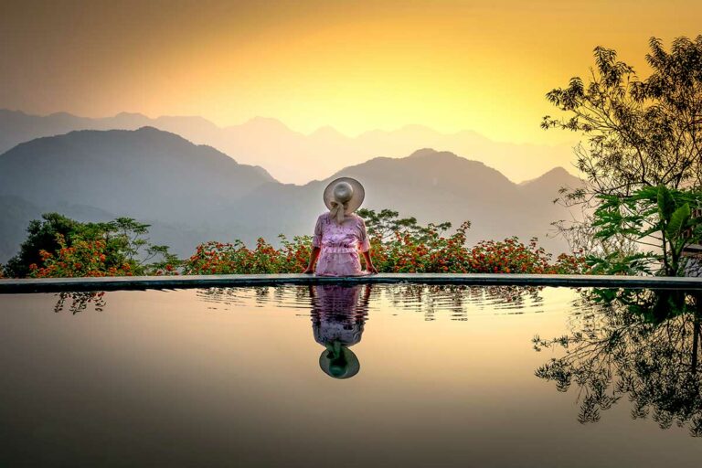 Zonsondergang bij Pu Luong Eco Garden met silhouetten van bergen, bloemen en een infinity pool die het landschap weerspiegelt