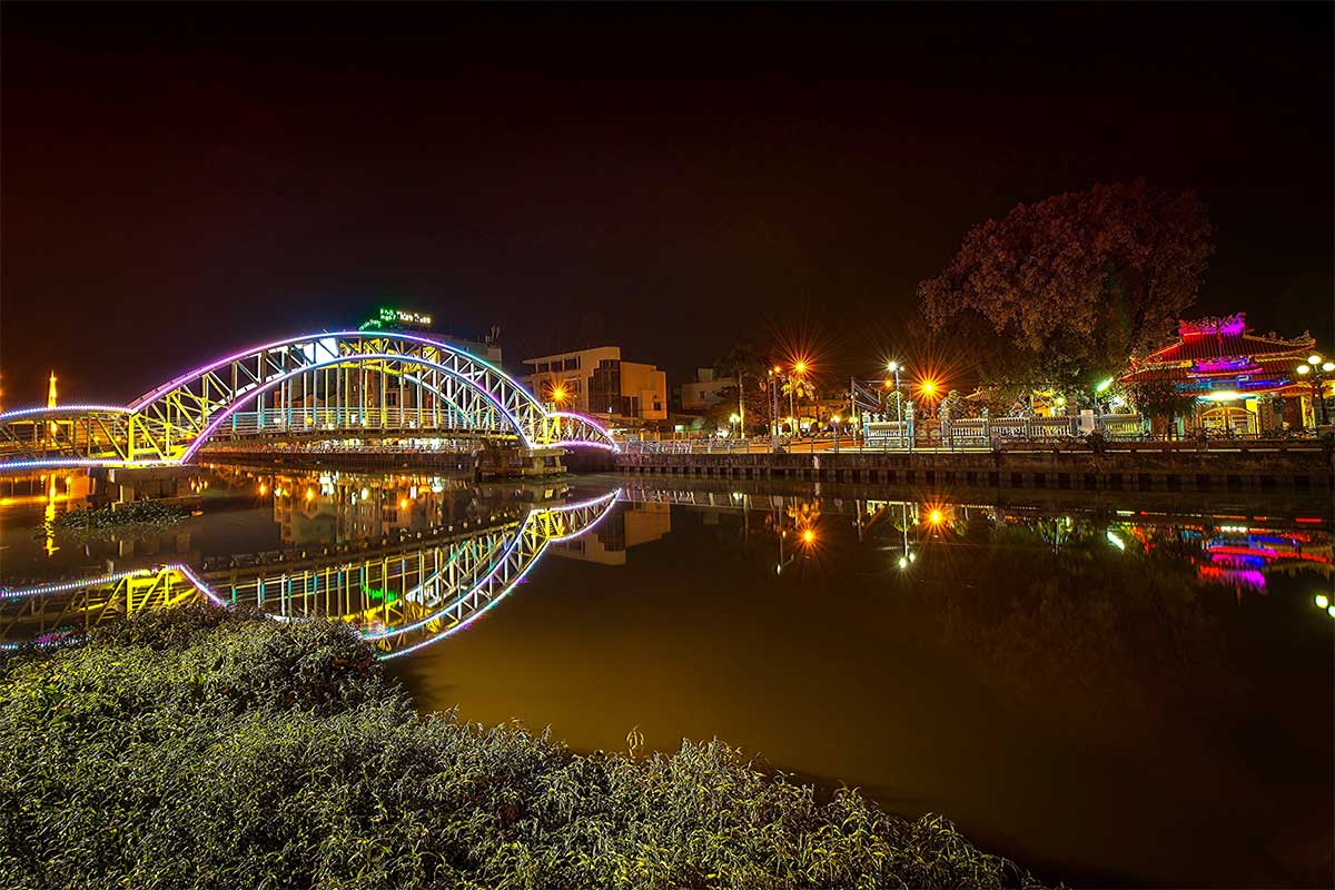 Verlichte brug en waterkant van Rach Gia in de avond met weerspiegeling in het kanaal